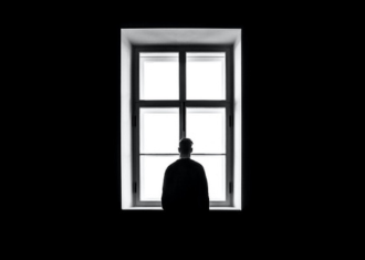 Fundo preto, com homem vestido de preto, á janela a refletir luz solar.