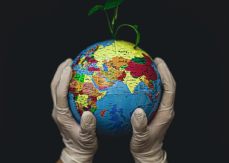 mãos com luvas brancas a segurar o mundo, de onde nasce uma planta.