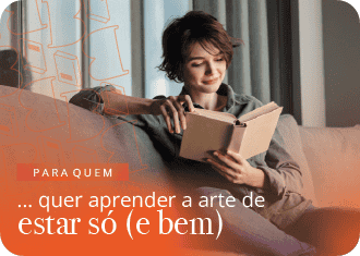 Senhora a ler livro sentada no sofá enquanto sorri.
