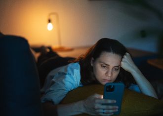 Adolescente deitada com o telemóvel na mão, com uma expressão triste e uma árvore de natal como fundo.