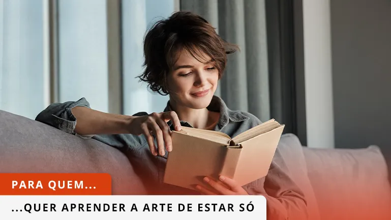 Senhora a ler livro sentada no sofá enquanto sorri.