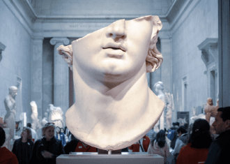 Representação de uma escultura, com a cabeça cortada, onde é visivel parte do cabelo, nariz e boca do busto. Exposta num museu.